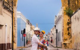 couple wearing traditional clothing hugging in front of the merida arch uxmal mexico